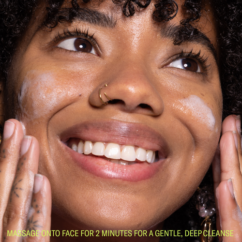 Woman smiling with face cleanser foam on face and clean skin
