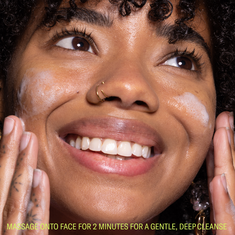 Woman smiling with face cleanser foam on face and clean skin