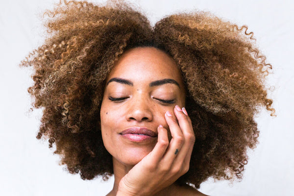 a woman with dark skin and an agro touching her face - benefits of castor oil 